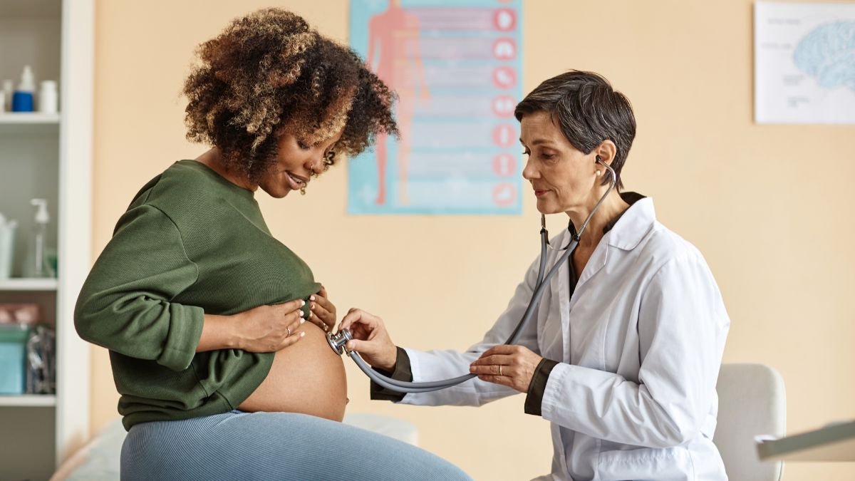 Eine schwangere Frau wird von einer Ärztin untersucht, während sie ihren Bauch hält.