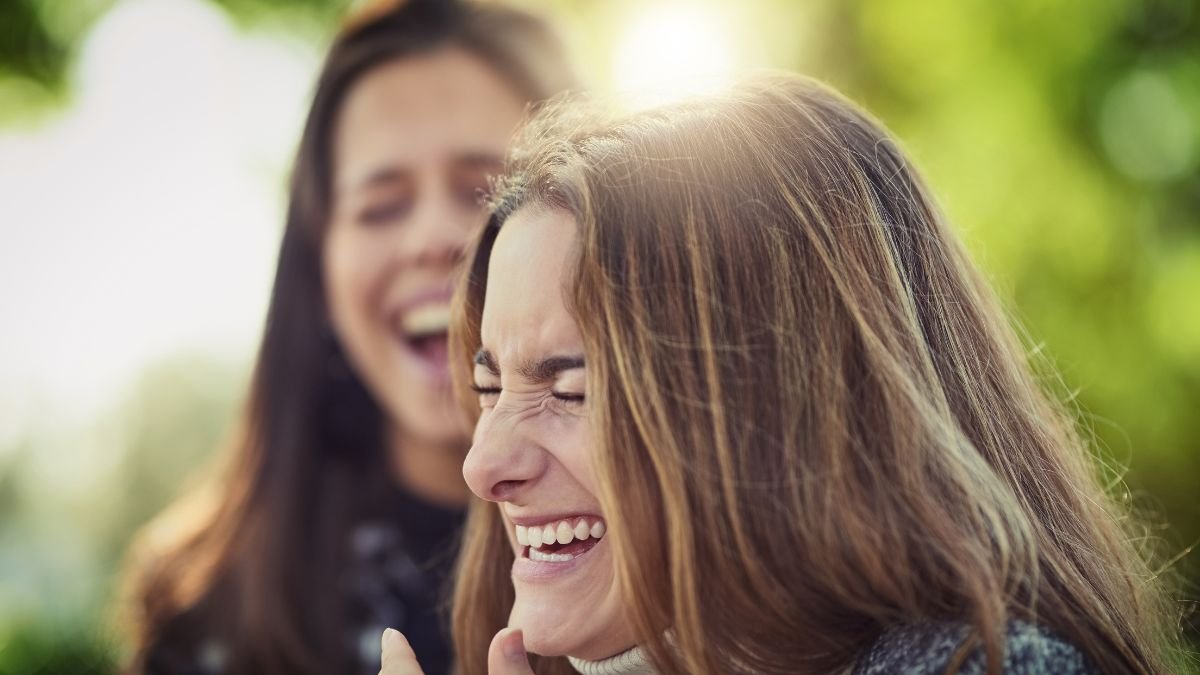 Zwei Frauen lachen herzlich im Freien, was Freude und Lebensfreude ausstrahlt.