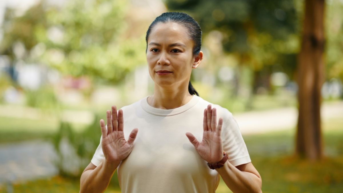 Eine Person praktiziert Tai Chi im Freien mit ruhiger Haltung und konzentrierter Mimik.
