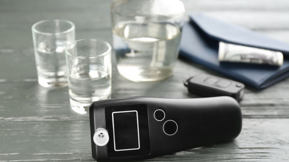Ein digitales Alkoholmessgerät liegt auf einem Tisch neben Gläsern mit Wasser.