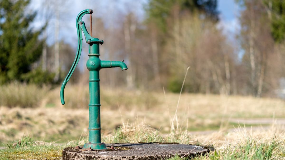 Eine grüne Handpumpe steht auf einem Betonfundament in einer natürlichen Umgebung.