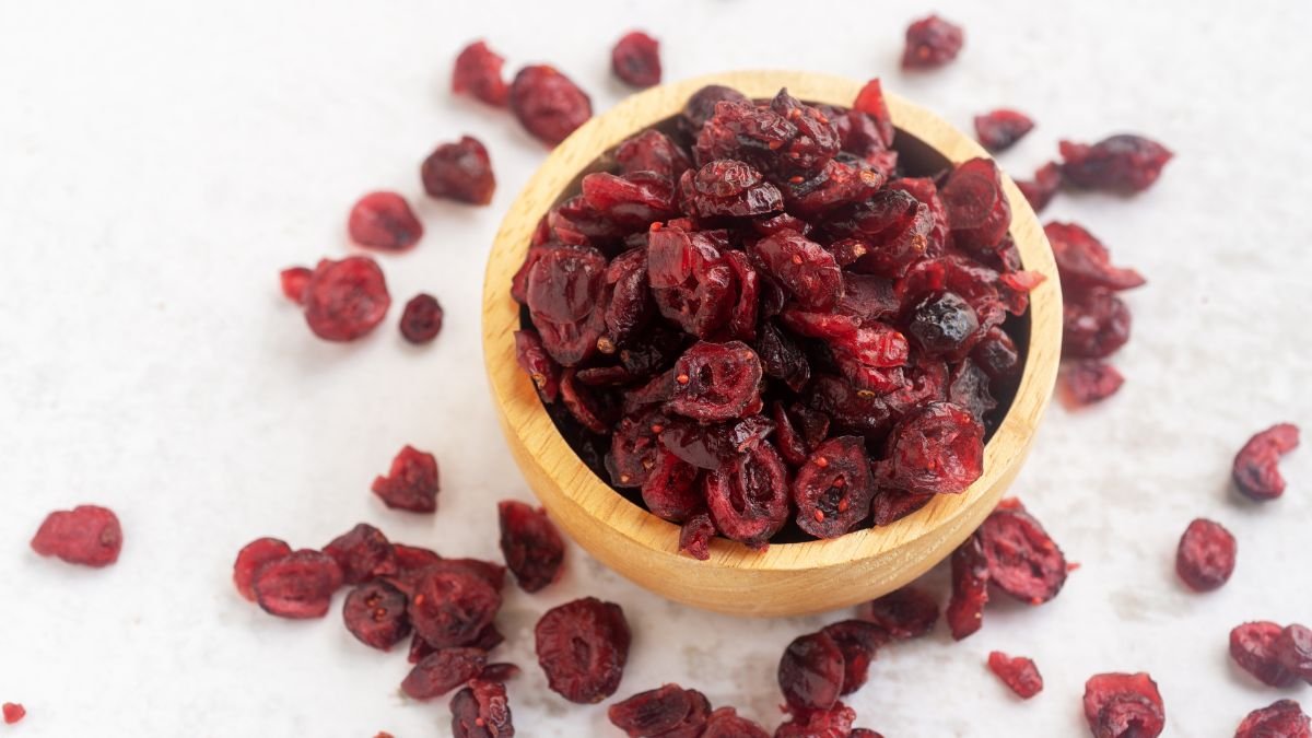 Eine Holzschale mit getrockneten Cranberries, umgeben von weiteren Cranberries.