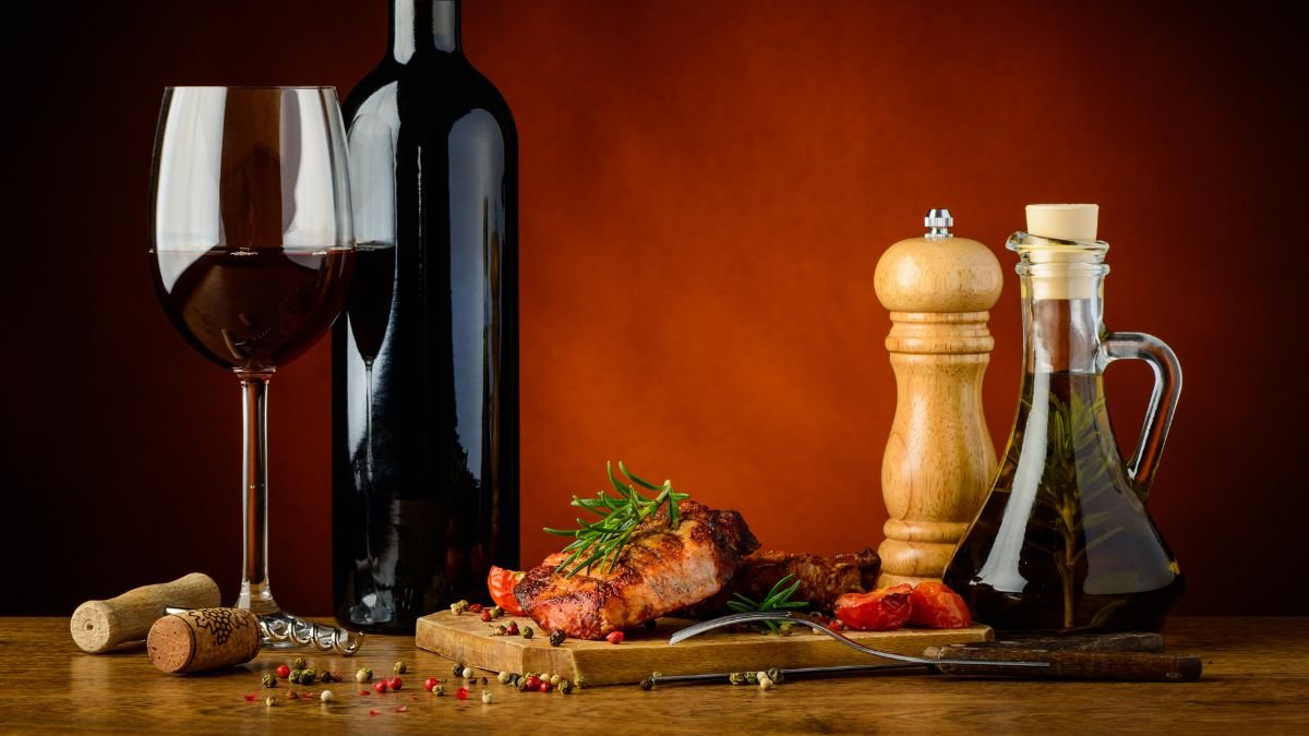 Ein Glas Rotwein, eine Flasche Wein, gegrilltes Fleisch und Gewürze auf einem Tisch.