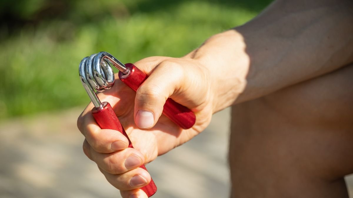 Eine Hand hält einen Handtrainer mit roten Griffen im Freien.