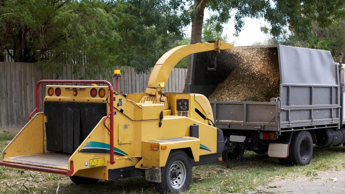 Ein gelber Holzschredder zerkleinert Gartenabfälle und lädt sie in einen Lkw.
