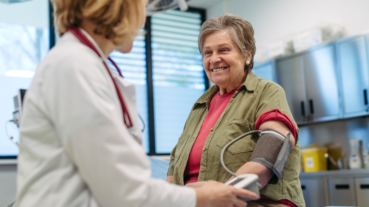 Eine ältere Frau lächelt während der Blutdruckmessung in einer Arztpraxis.