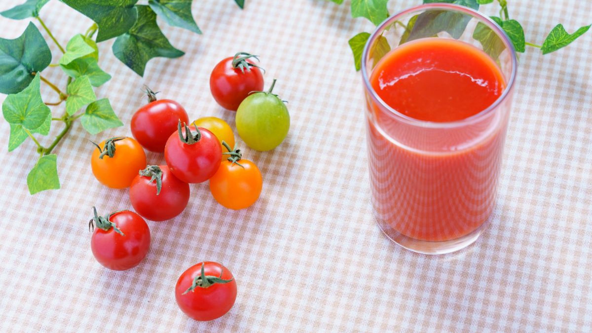 Ein Glas Tomatensaft neben frischen, bunten Kirschtomaten auf einem Tisch.