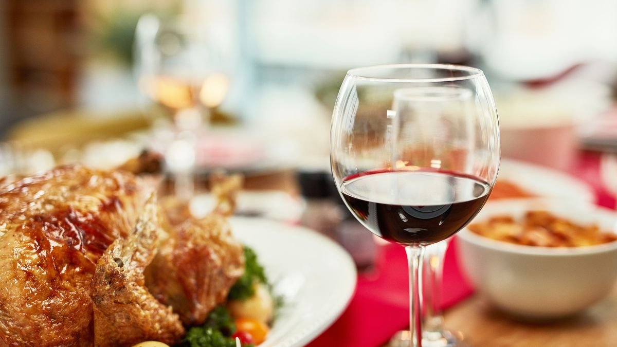 Ein Glas Rotwein steht neben einem köstlichen Braten und buntem Gemüse.