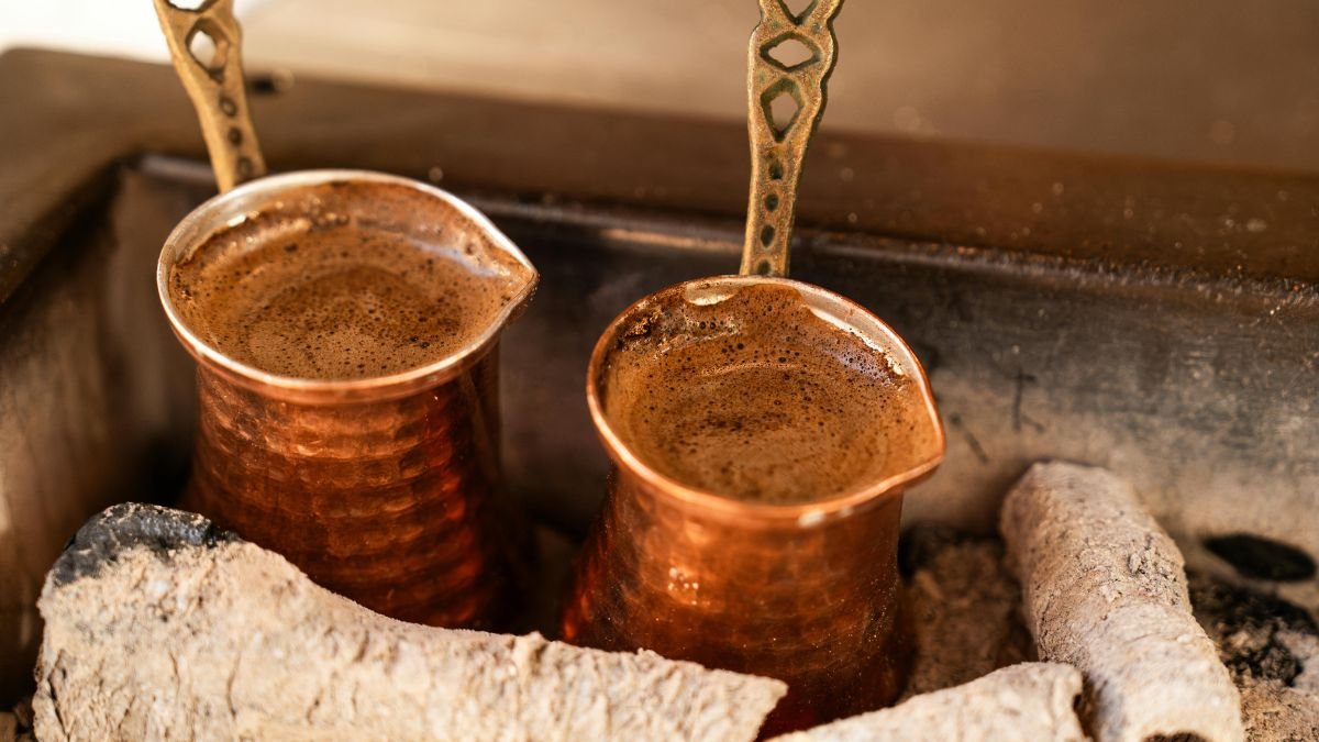 Zwei kupferne Kaffeekannen mit dampfendem Kaffee auf glühenden Kohlen.