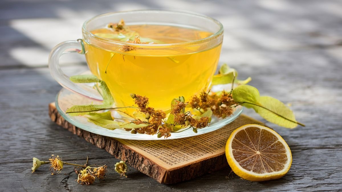 Eine Tasse Lindenblütentee mit frischen Blüten und einer Zitronenscheibe.