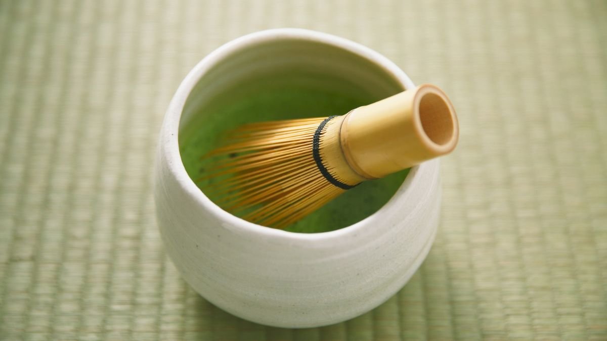 Eine Schale mit grünem Matcha-Tee und einem traditionellen Bambusbesen.