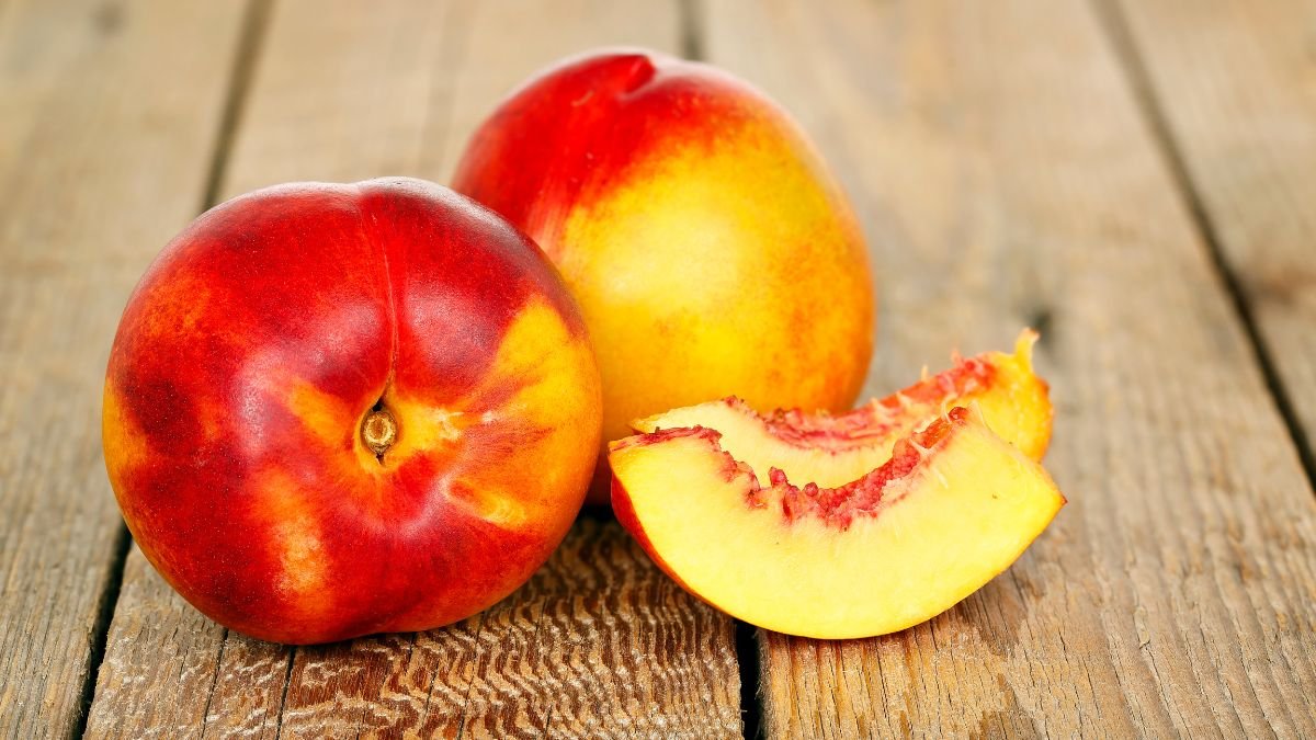 Zwei reife Nektarinen und ein Stück auf einem Holztisch.