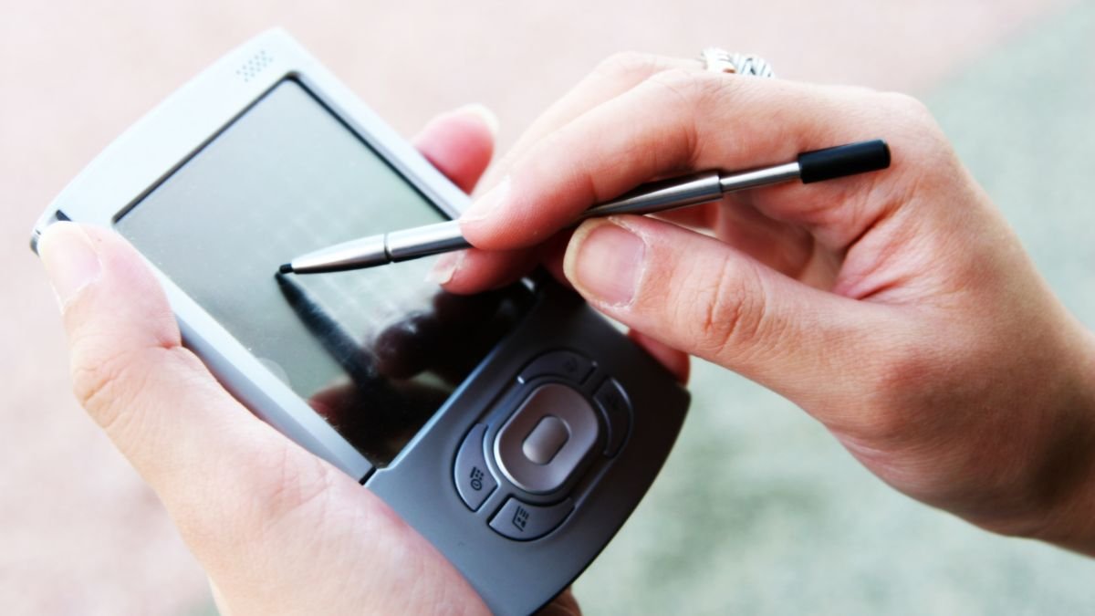 Eine Hand hält einen PDA mit einem Stylus auf dem Bildschirm.