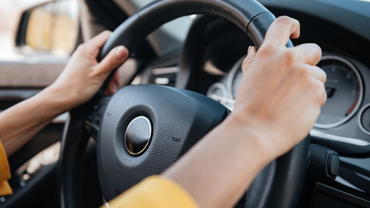 Hände halten ein Lenkrad in einem modernen Auto, bereit zum Fahren.