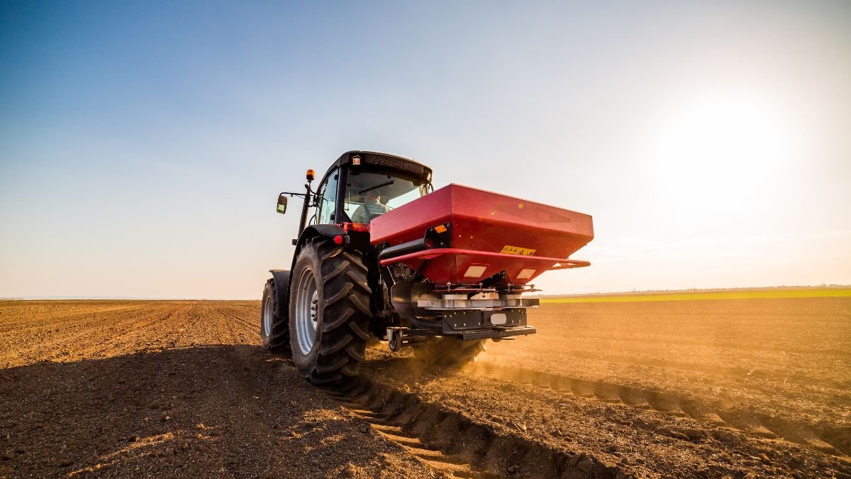 Ein Traktor verteilt Stickstoffdünger auf einem Feld bei Sonnenuntergang.