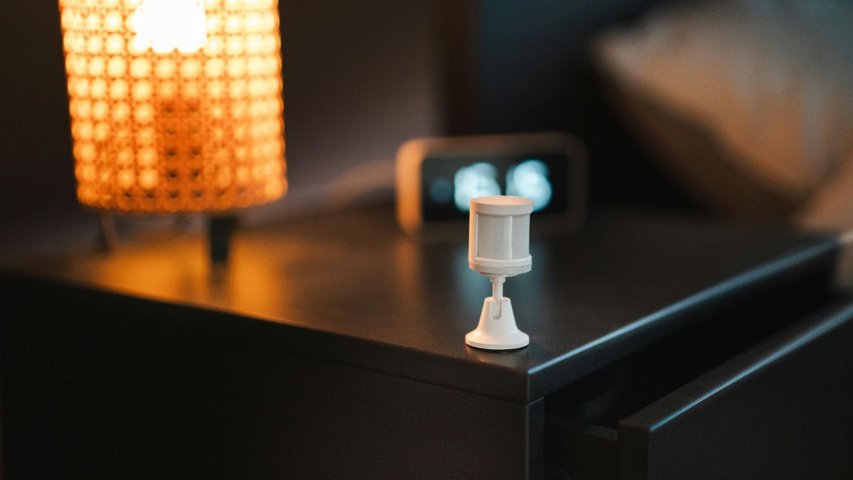Ein Temperatursensor steht auf einem Nachttisch neben einer Lampe und einer Uhr.