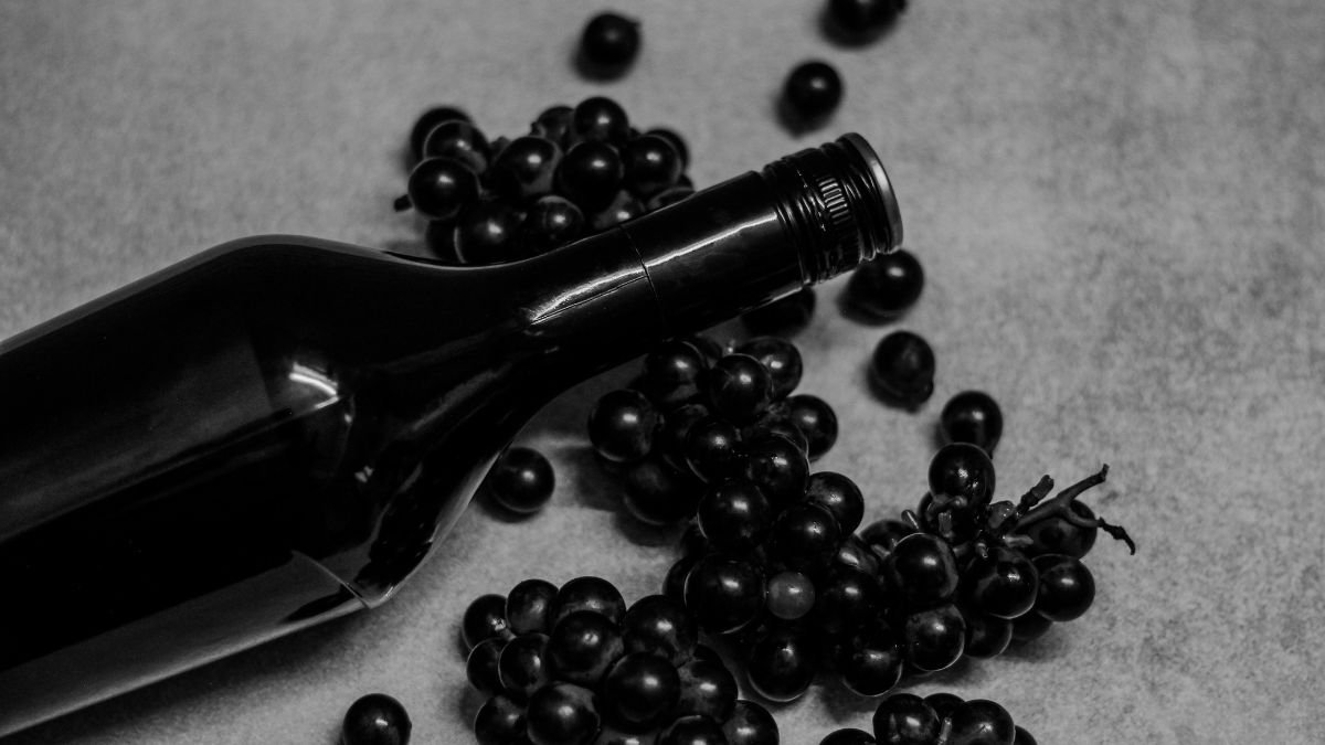 Eine Flasche Rotwein liegt neben frischen, dunklen Trauben auf einem Tisch.