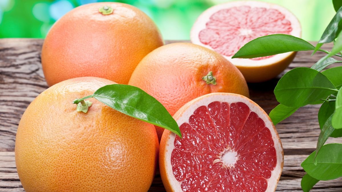 Frische Grapefruits liegen auf einem Holztisch, eine ist aufgeschnitten.
