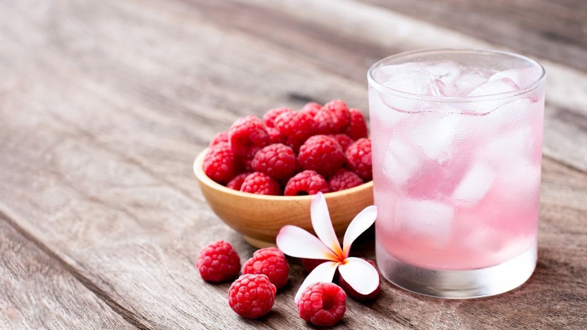 Ein Glas mit einem rosa Getränk und frischen Himbeeren auf einem Holztisch.