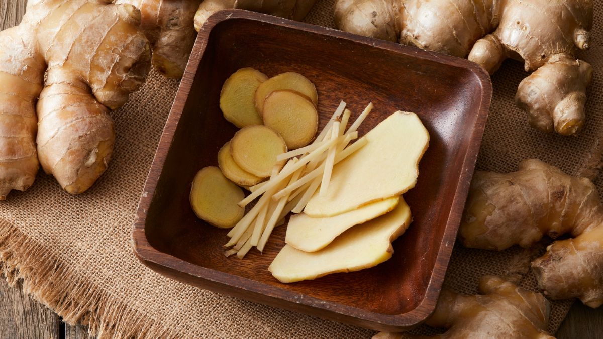 Frische Ingwerstücke in einer Holzschale, umgeben von Ingwerknollen.