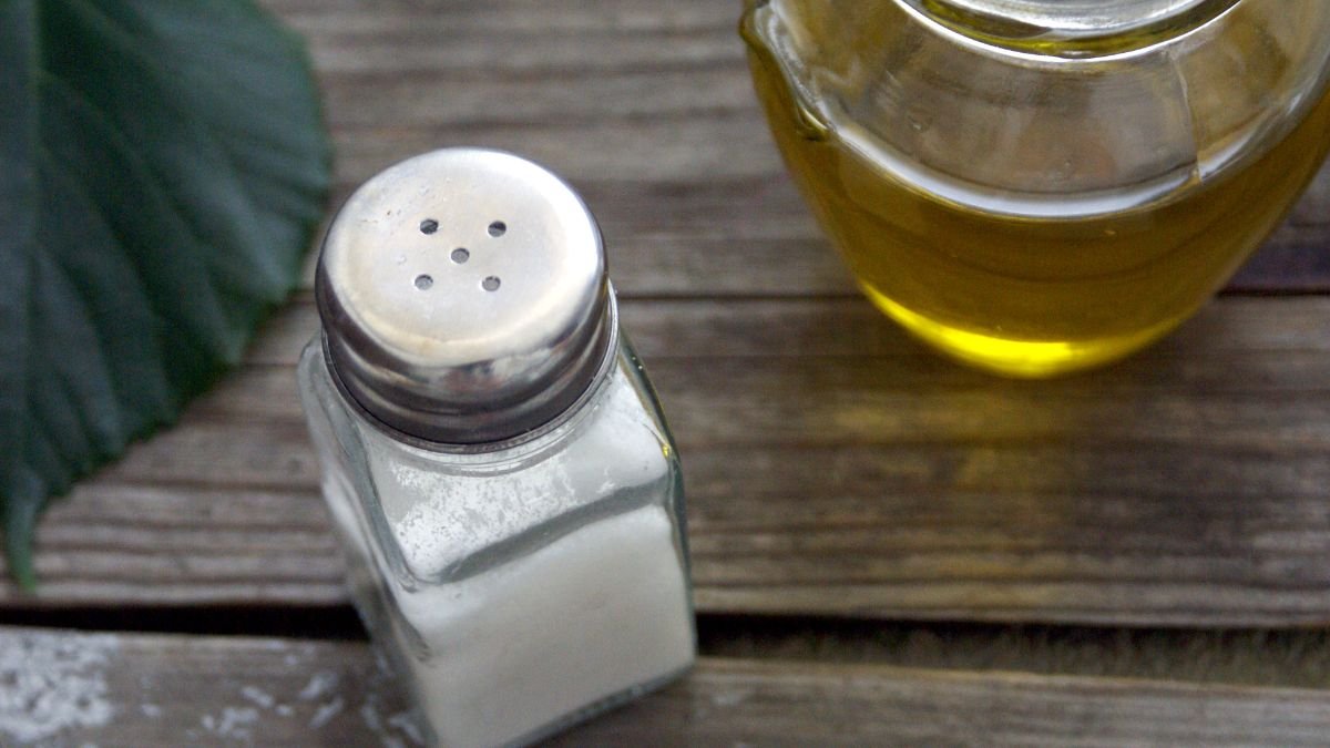 Ein Salzstreuer steht neben einer Glasflasche mit Öl auf einem Holztisch.