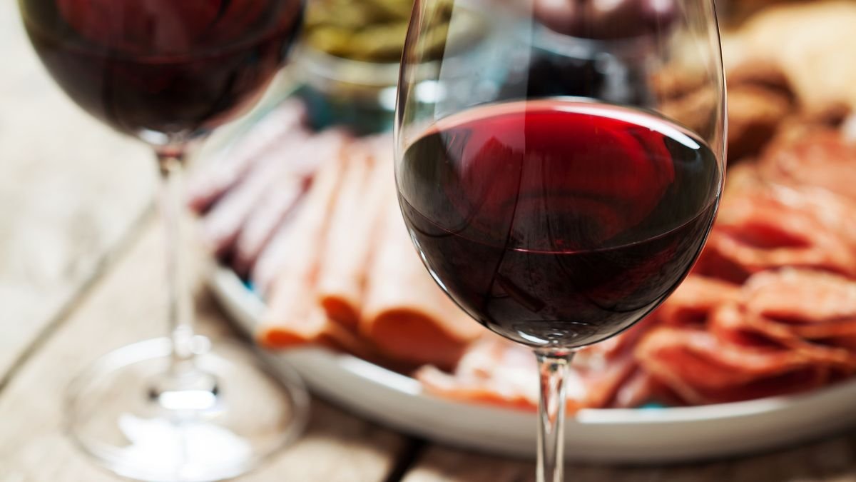 Zwei Gläser Rotwein vor einem Teller mit verschiedenen Wurstsorten.