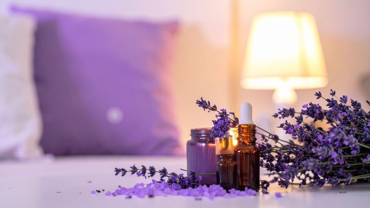 Drei Fläschchen ätherischer Öle und Lavendelblüten auf einem Tisch.