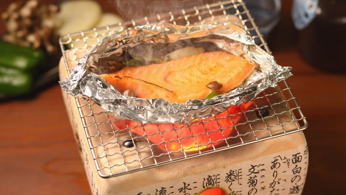 Ein Stück Lachs in Alufolie auf einem Grill, umgeben von Gemüse.