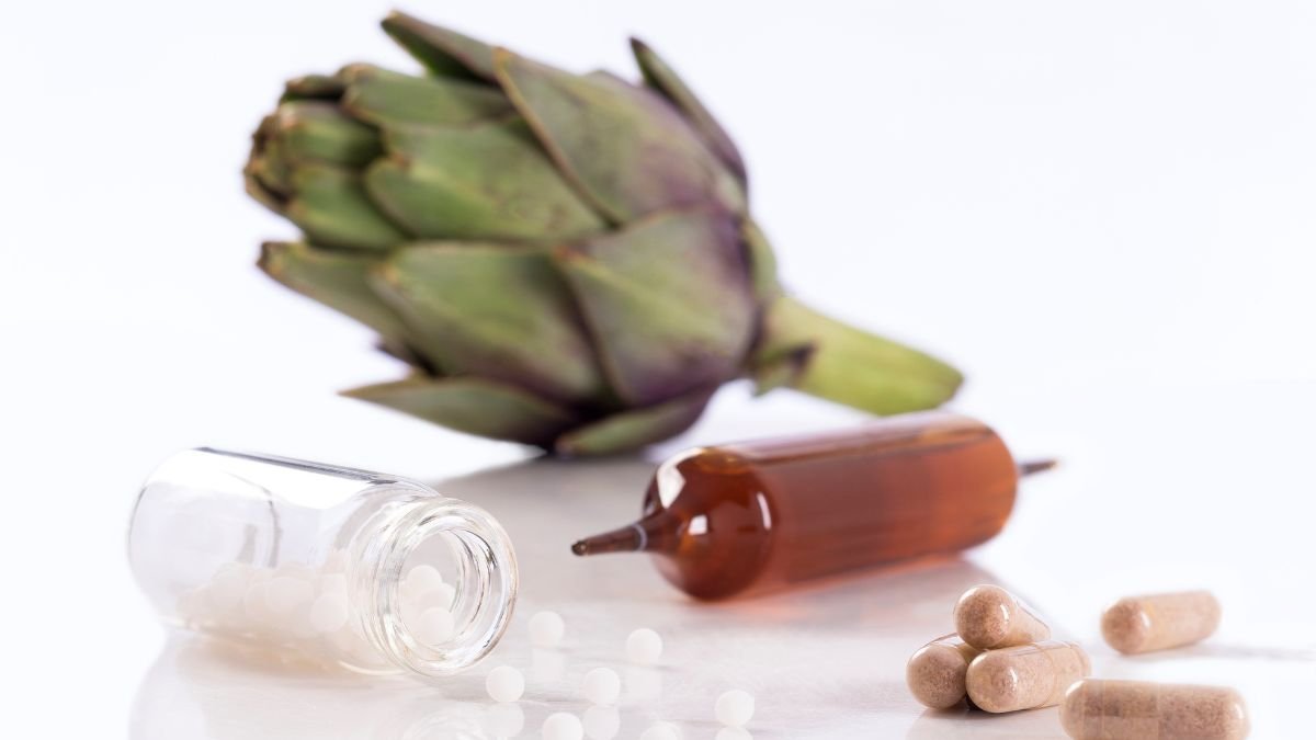 Eine Artischocke neben einer offenen Flasche mit homöopathischen Kügelchen und Kapseln.
