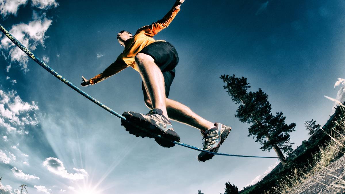 Ein Sportler balanciert auf einem Seil in der Natur unter blauem Himmel.