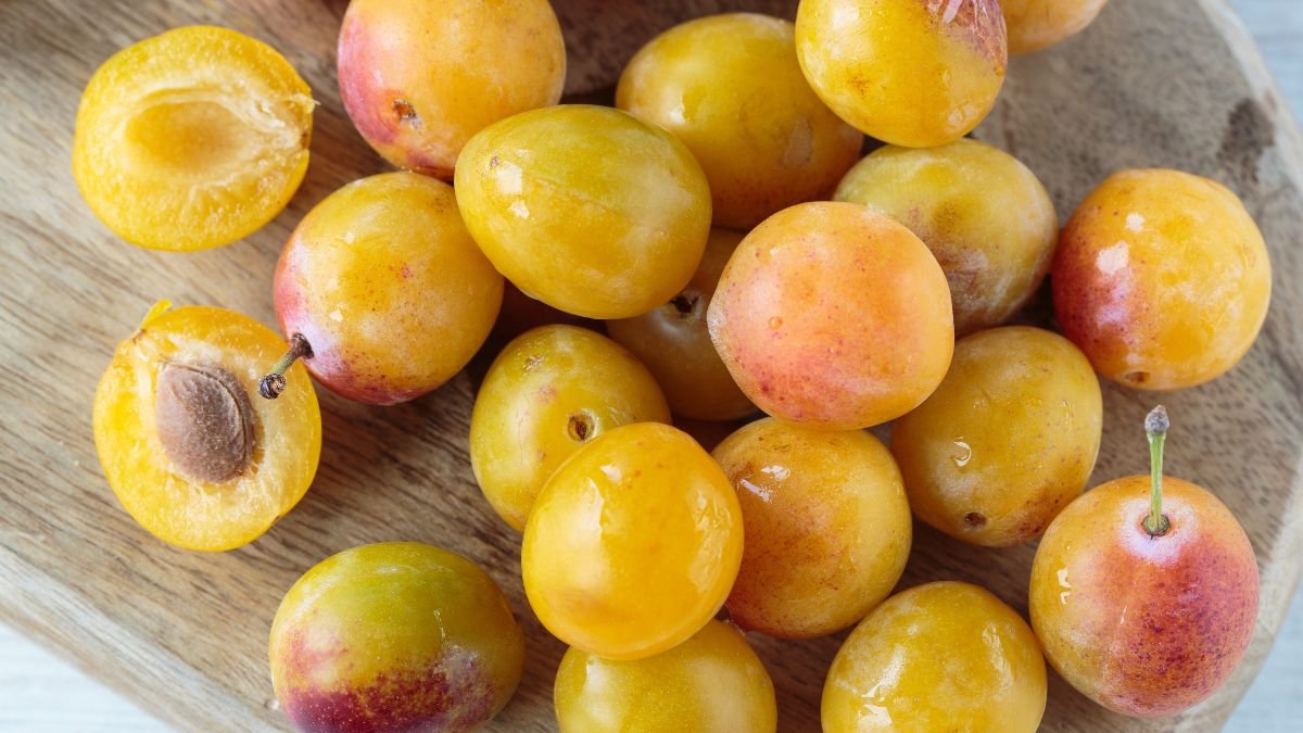 Eine Auswahl frischer Mirabellen auf einem Holzbrett, einige halbiert.