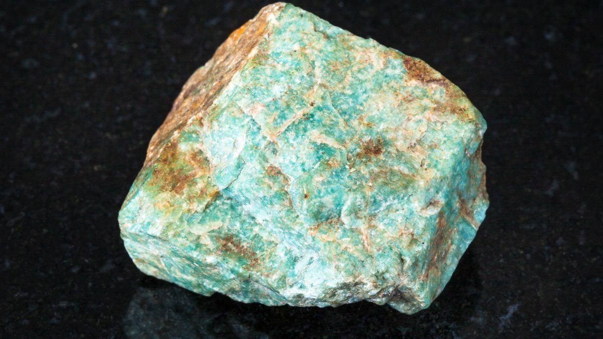 Ein ungeschliffenes Stück Amazonit mit grüner und blauer Farbe auf schwarzem Hintergrund.