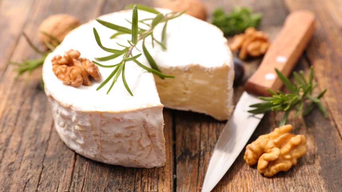 Ein Stück Camembert-Käse mit Walnüssen und frischen Kräutern auf einem Holzbrett.