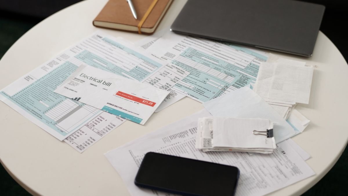 Ein Tisch mit verschiedenen Rechnungen, darunter eine Stromrechnung und ein Smartphone.