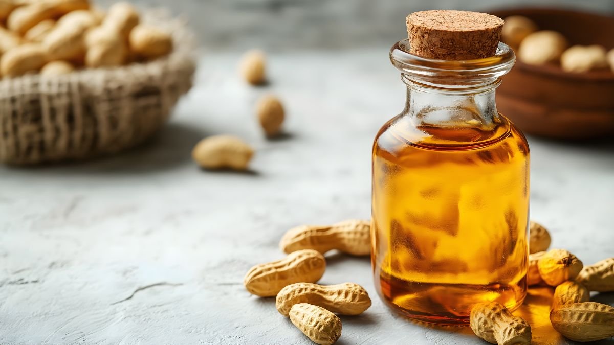 Eine Flasche Erdnussöl umgeben von Erdnüssen auf einem hellen Hintergrund.