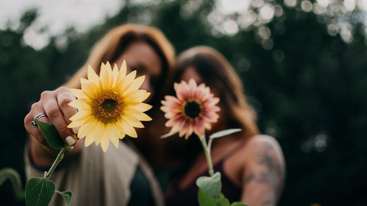 Zwei Frauen halten Sonnenblumen in der Hand, umgeben von Natur.