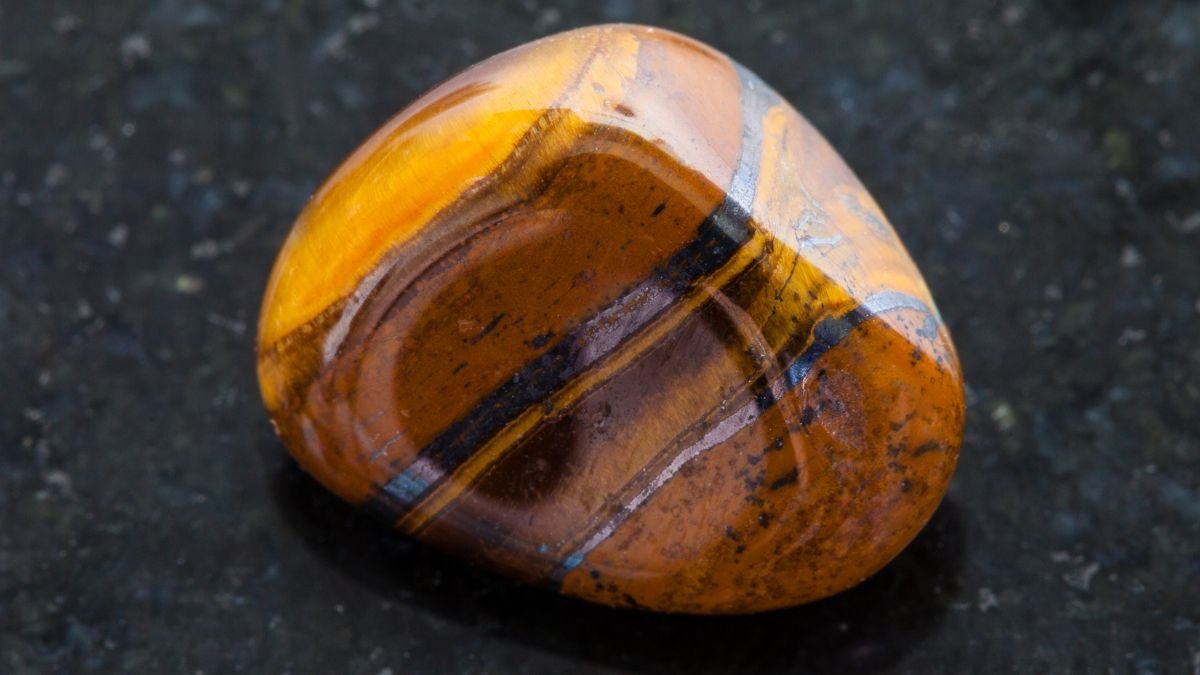 Ein glatter Falkenauge-Stein mit goldbraunen und blauen Streifen auf schwarzem Hintergrund.