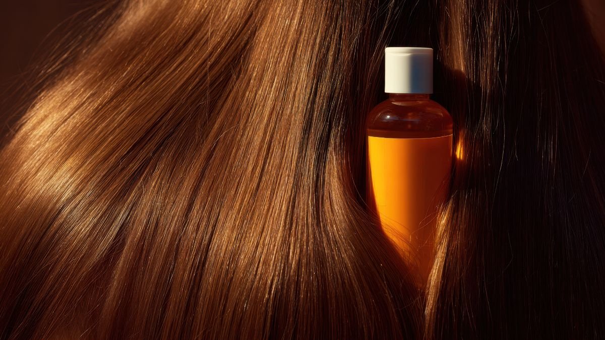 Eine Flasche mit orangefarbener Flüssigkeit zwischen glänzendem Haar.