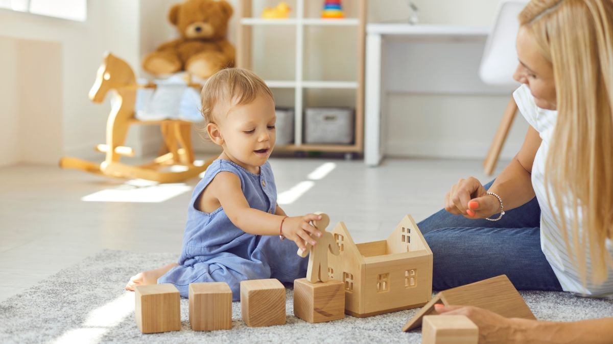 Ein Kleinkind spielt mit Holzspielzeug auf einem Teppich in einem hellen Raum.