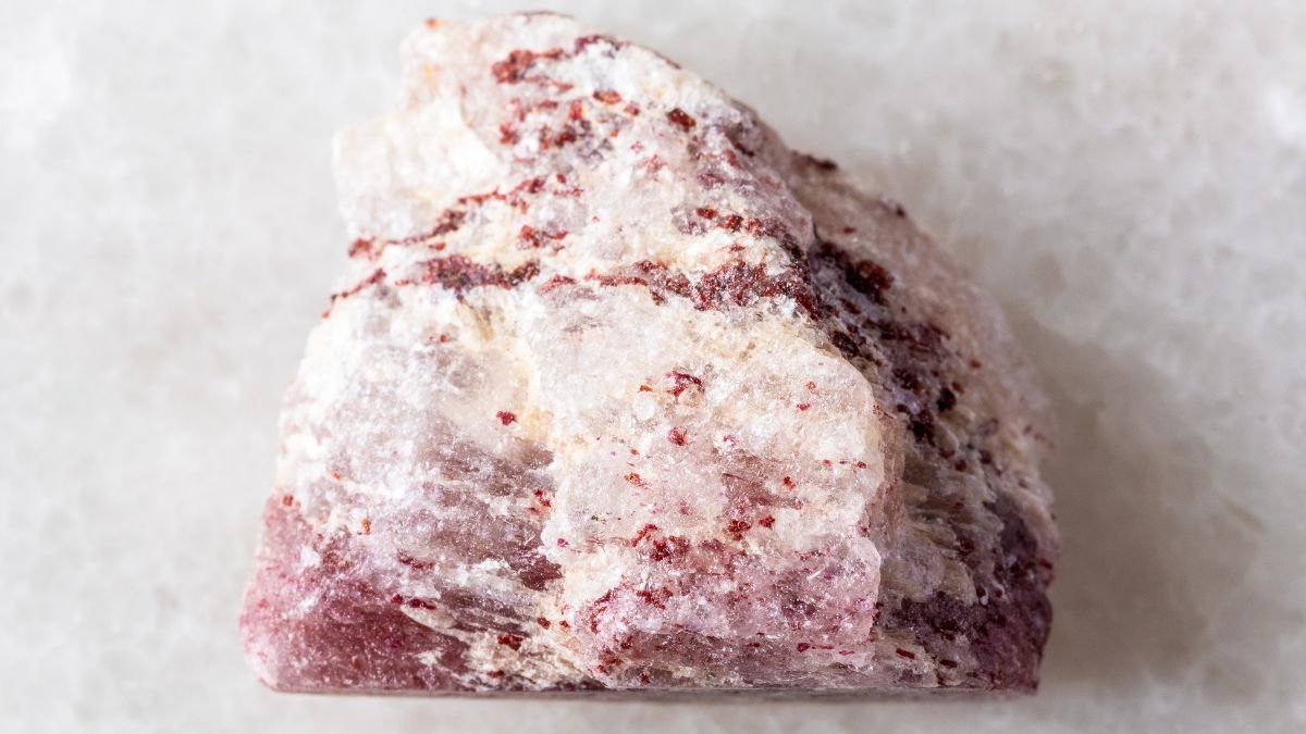 Ein Stück Erdbeerquarz mit rötlichen Einschlüssen auf hellem Hintergrund.