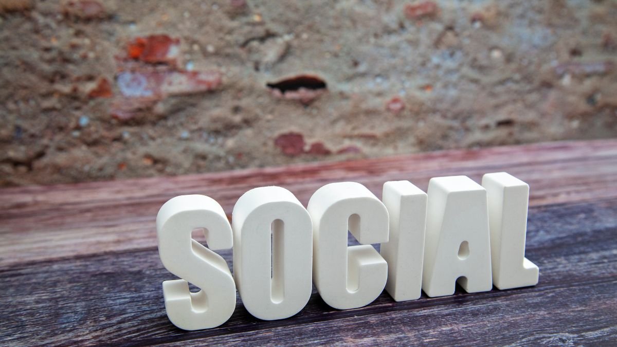 Weiße Buchstaben bilden das Wort 'SOCIAL' auf einem Holztisch.