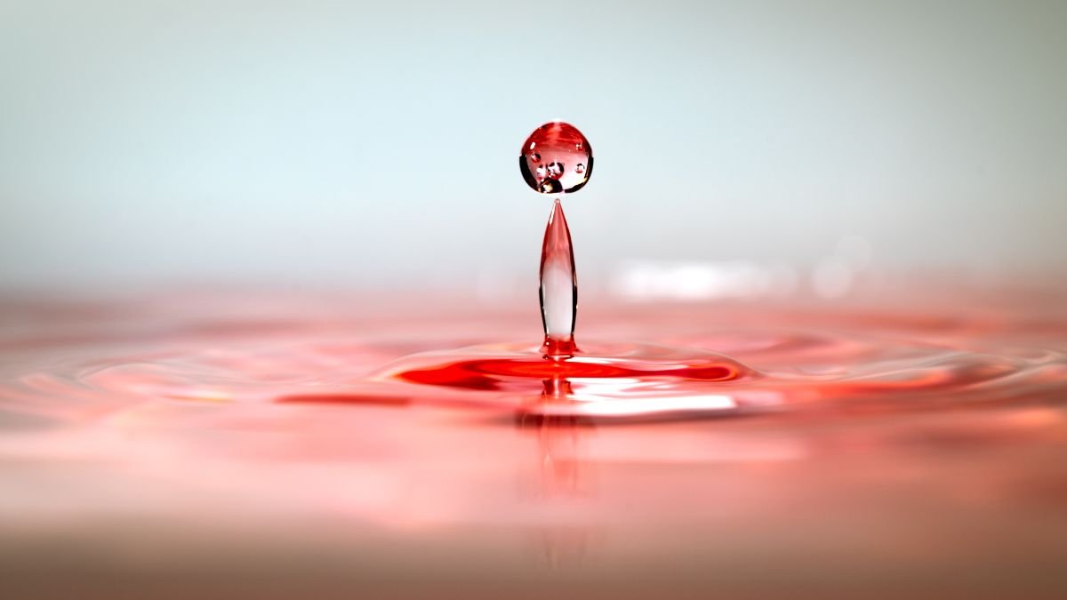 Ein Wassertropfen, der in rotem Wasser schwebt und eine Welle erzeugt.