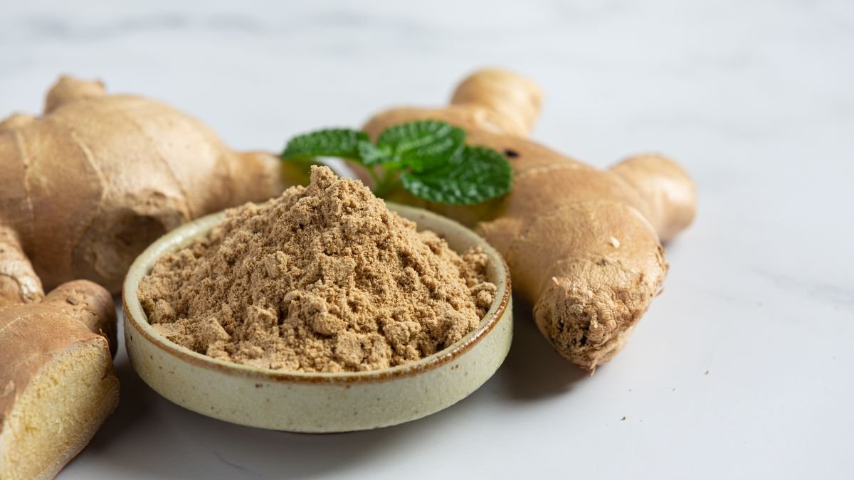 Eine Schale mit Ingwerpulver neben frischem Ingwer und Minzblättern.