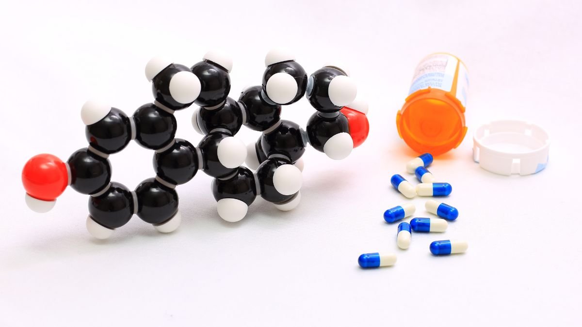 Molekülmodell von Ethinylestradiol neben einer offenen Medikamentenflasche und Kapseln.