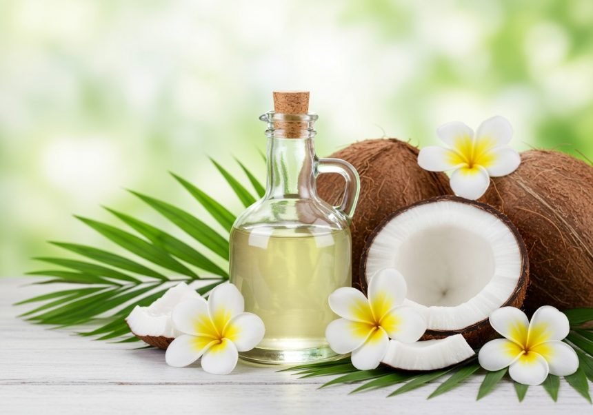 Eine Flasche Kokosöl steht neben frischen Kokosnüssen und Blumen.