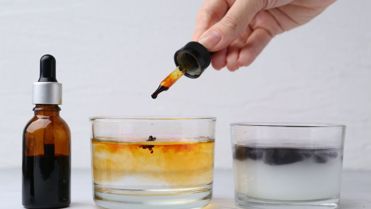 Eine Hand tropft Jod in ein Glas Wasser, während zwei Flaschen daneben stehen.