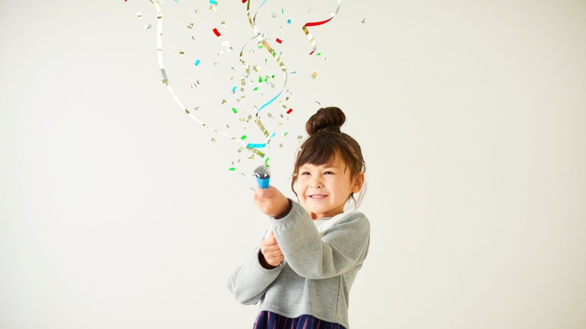 Ein fröhliches Kind zielt mit einer Konfetti-Kanone auf die Kamera.