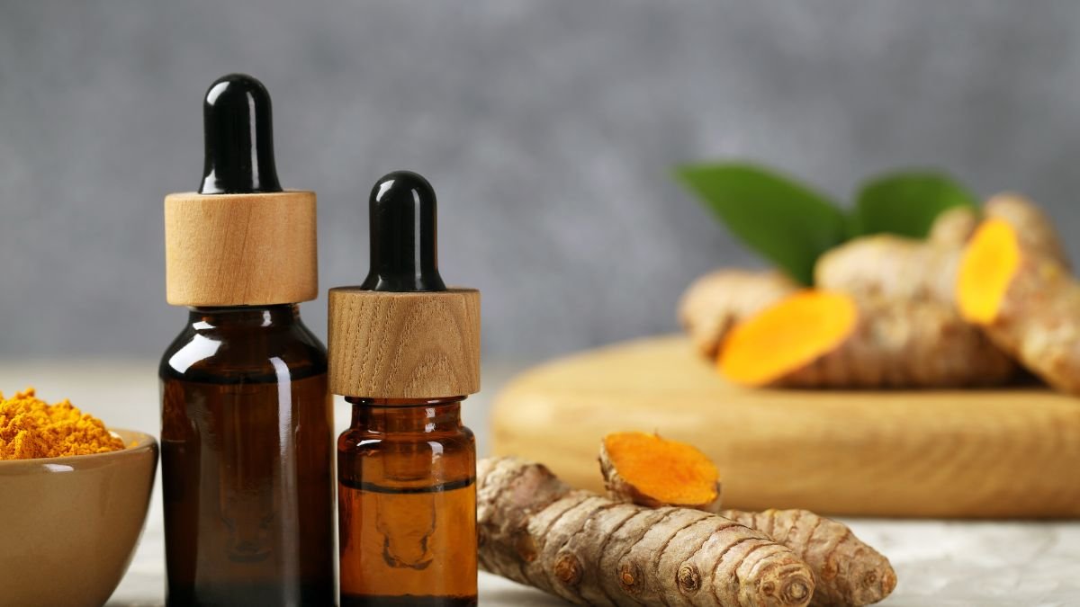 Zwei Fläschchen mit Kurkumaöl und frischer Kurkuma auf einem Tisch.
