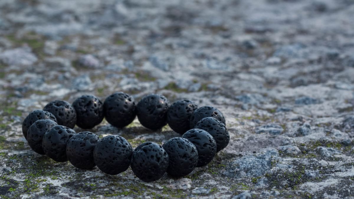 Ein schwarzes Lava-Armband aus natürlichen Lavasteinen auf einem grauen Untergrund.