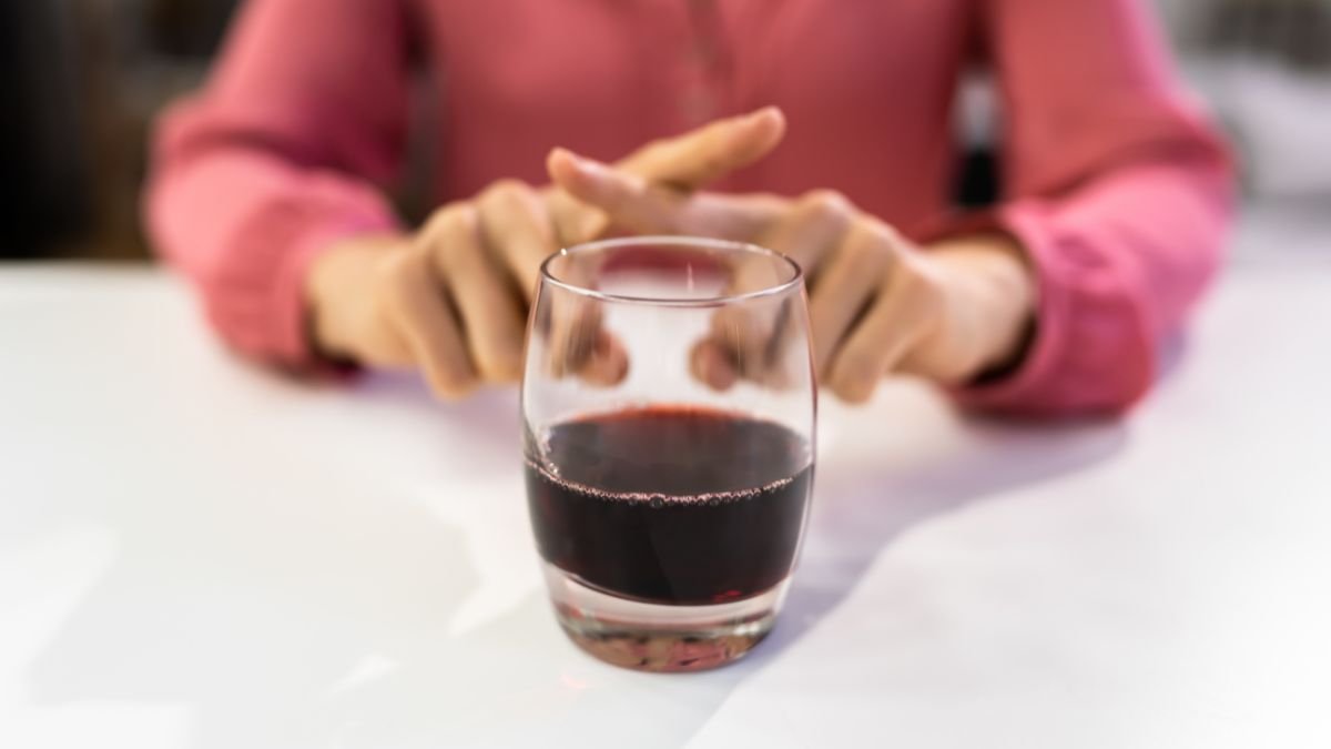 Ein Glas Rotwein steht auf einem Tisch, während eine Person die Hände darüber faltet.